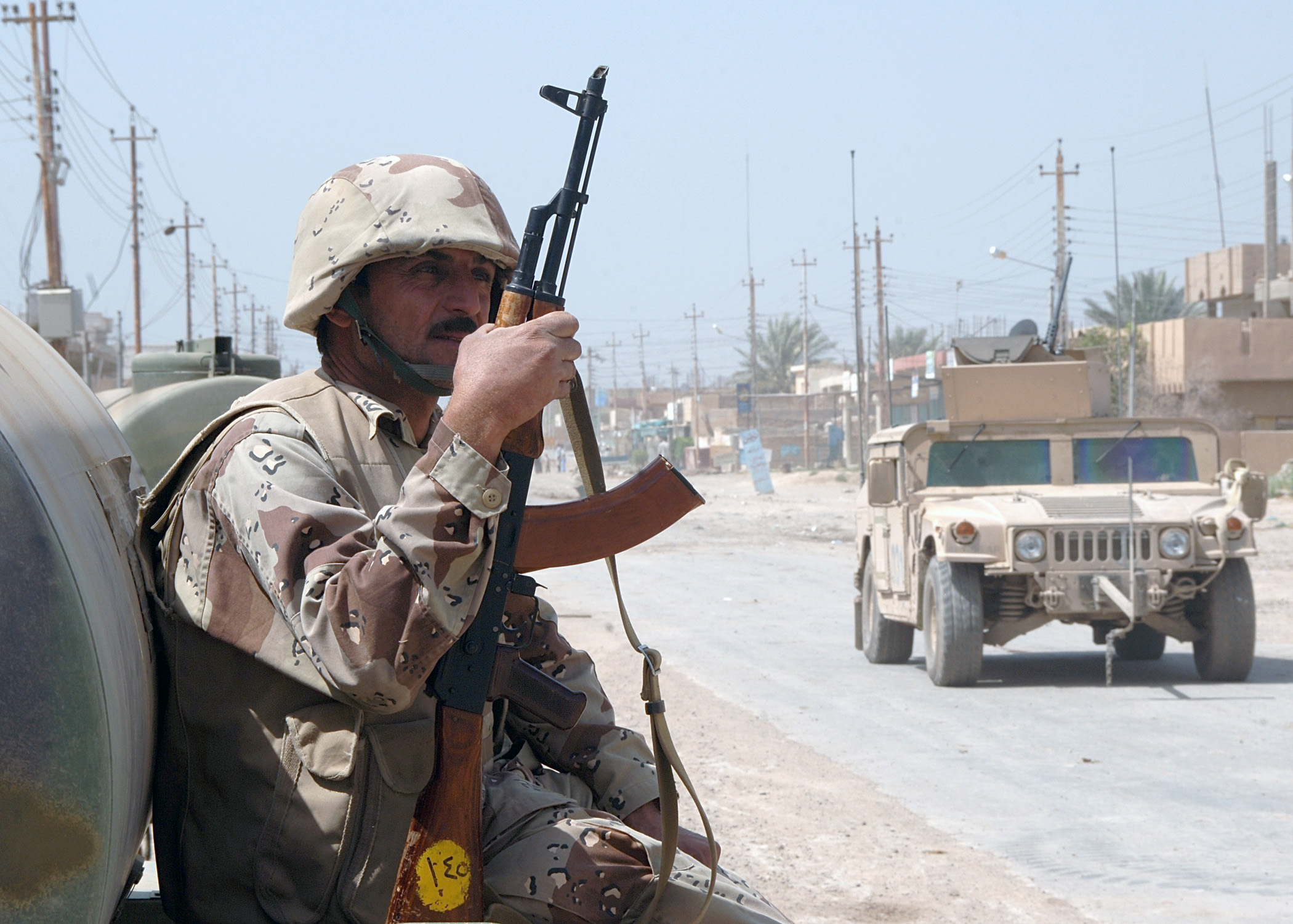 060325-N-6901L-039 Tarmiya, Iraq (March 25, 2006) - Iraqi soldier Zatar Jeba sits and watches a U.S. Army patrol drive by in their M1114 HMMWV (Humvee) vehicles during counter-insurgency operations. U.S. Navy photo by Photographer's Mate 1st Class Michael Larson (RELEASED)